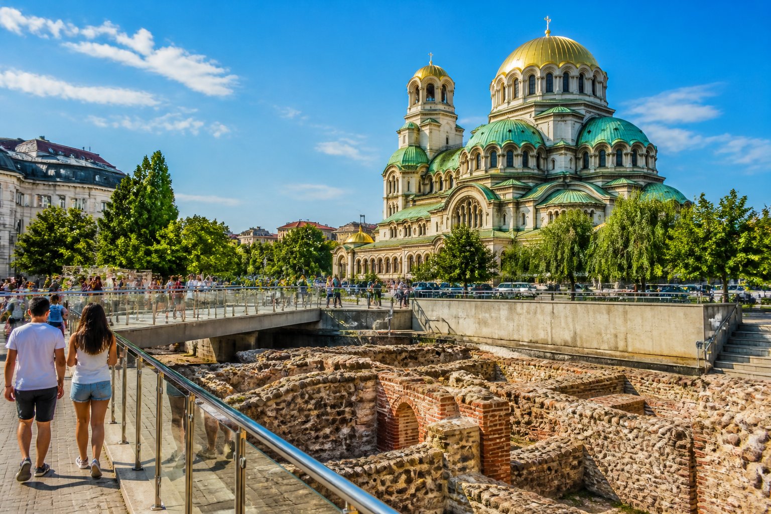 Vista de pontos turísticos icônicos de Sófia, Bulgária, incluindo a Catedral Alexander Nevsky e ruínas antigas, com pessoas caminhando e árvores ao redor.